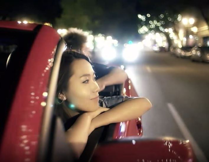 Asian woman looking happily out the side of a red open top convertible in the city